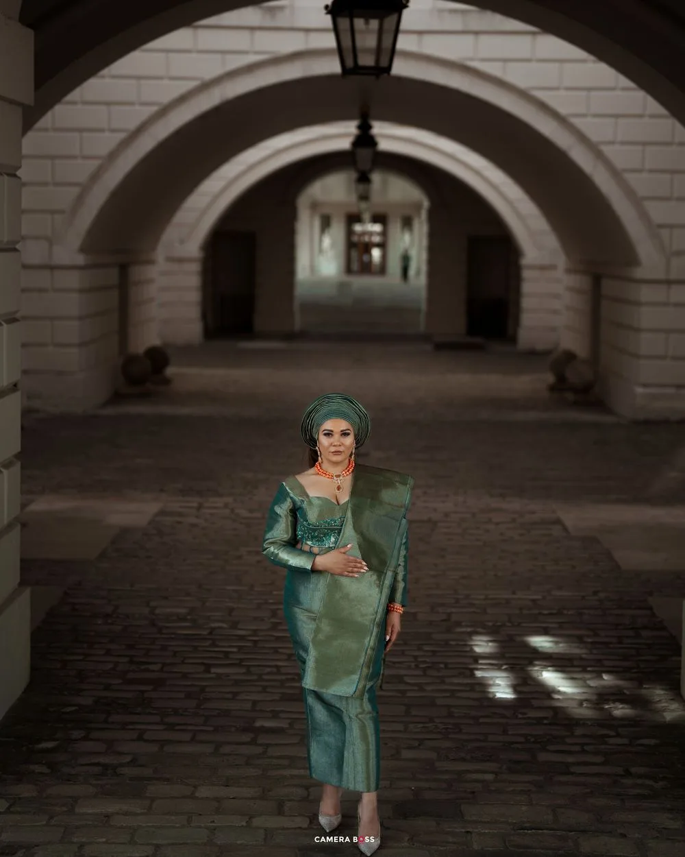 A person in a shimmering turquoise dress poses gracefully beneath a series of stone archways.
