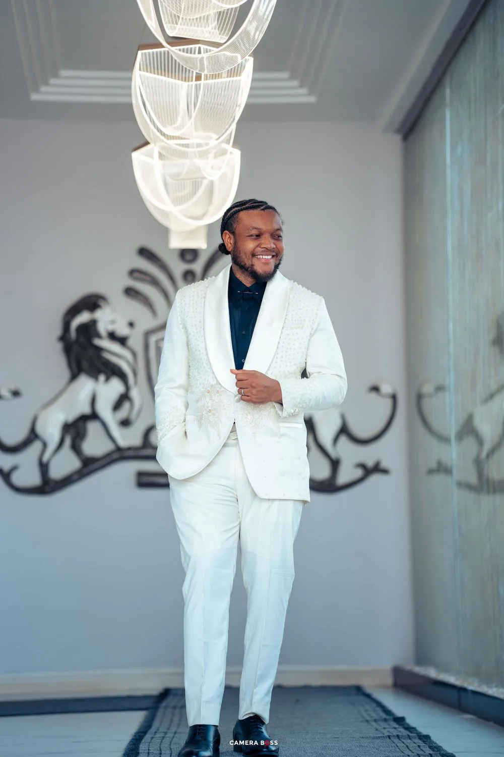 Someone wearing a crisp white suit and black turtleneck stands confidently in a modern interior with decorative wall art.
