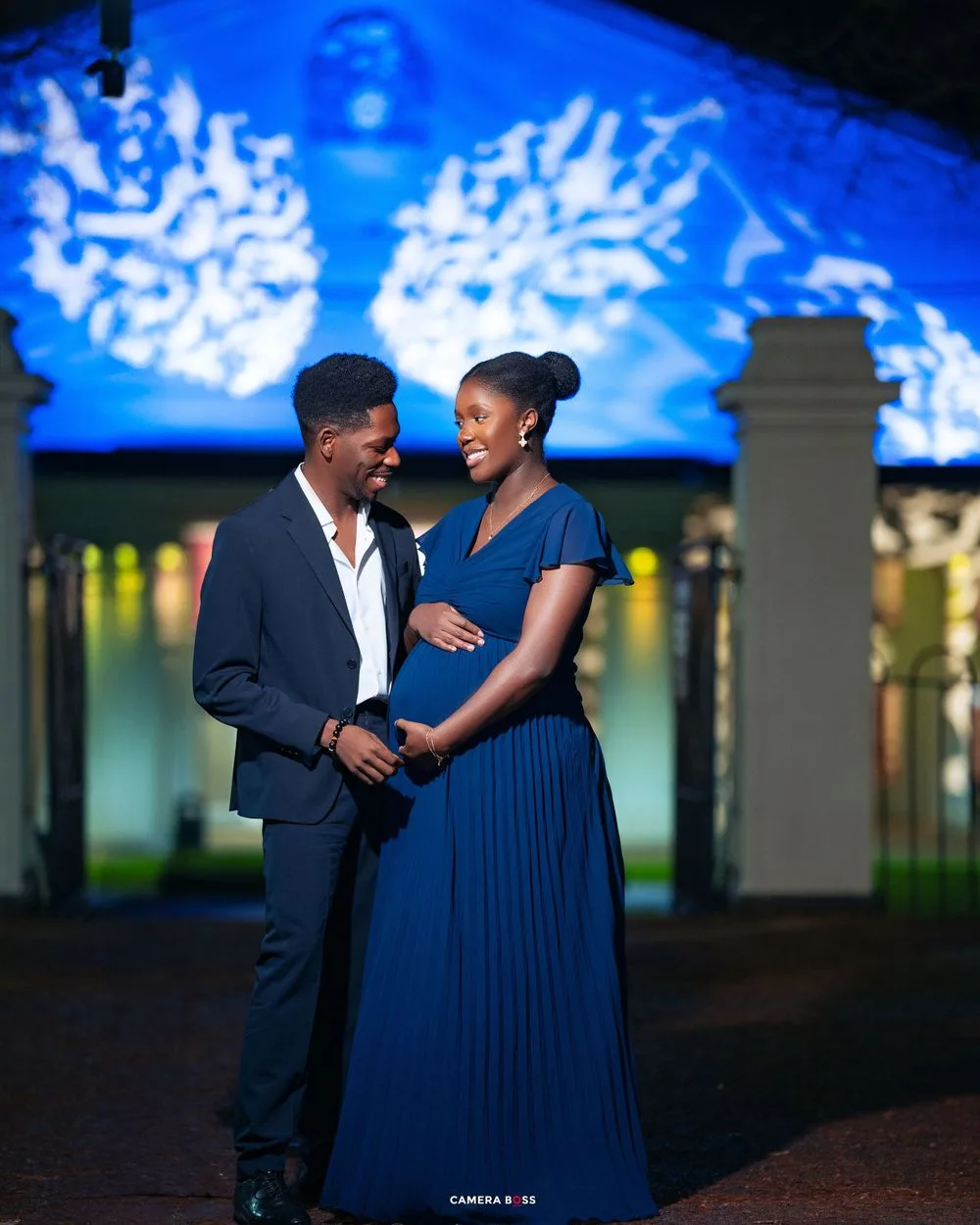 A couple shares a romantic moment at night under blue decorative lighting in an elegant outdoor setting.