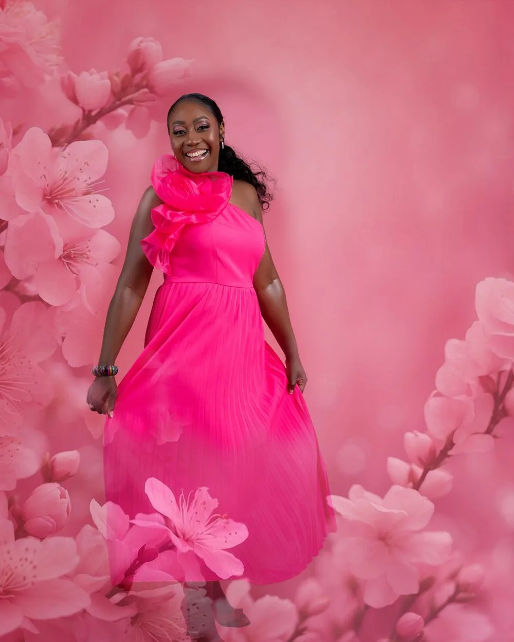 A figure in a bright pink flowy gown poses against a pink background with cherry blossom flowers framing the scene.