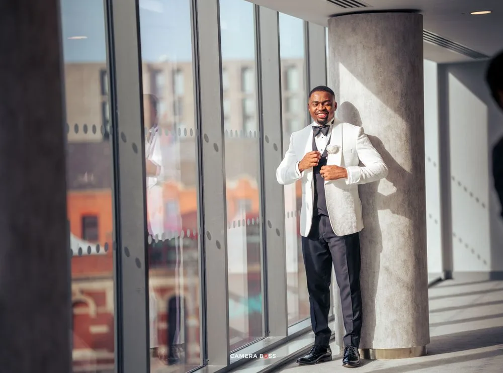 A person in a white jacket stands by large windows in a modern building interior.