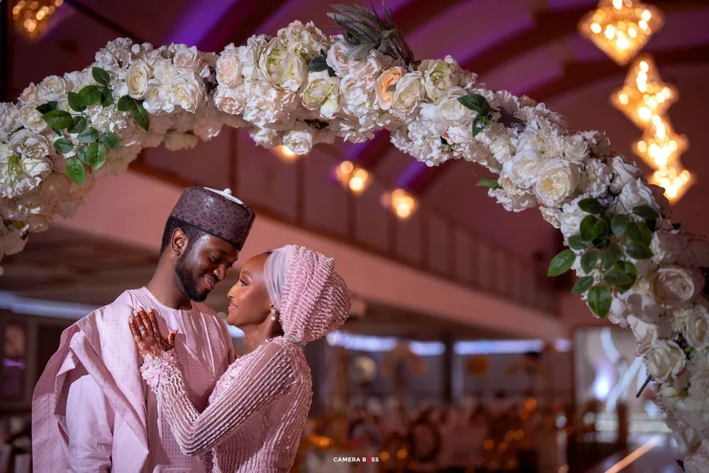 Wedding venue decorated with white floral arches and romantic purple ambient lighting.