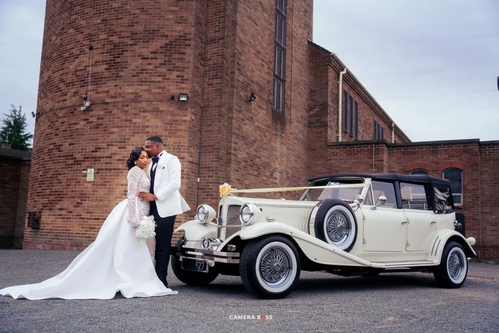 A classic cream-colored vintage Rolls Royce parked in front of a brick church serves as an elegant wedding backdrop.