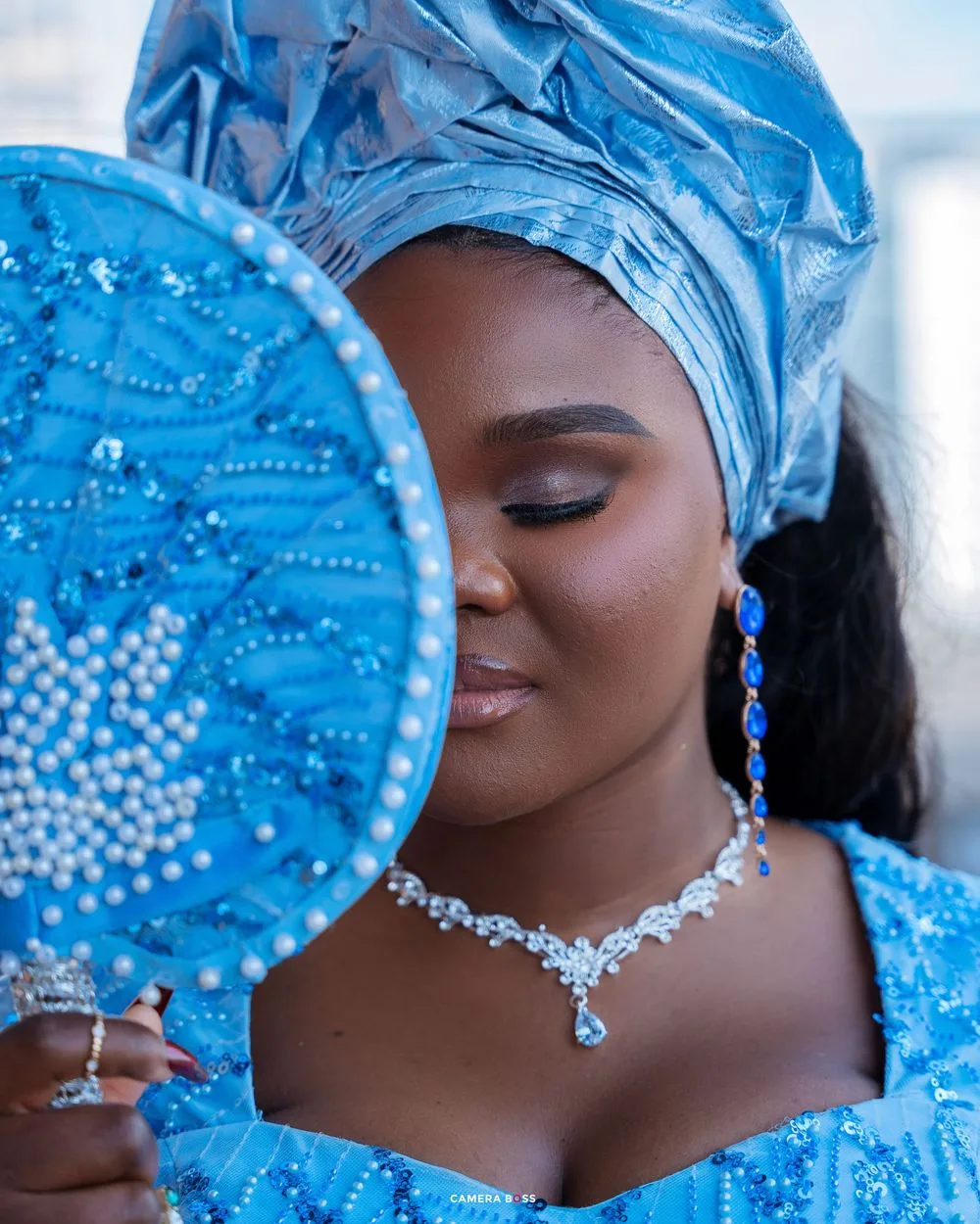Close-up portrait in elegant blue traditional attire with matching headwrap and sparkling crystal necklace and accessories.