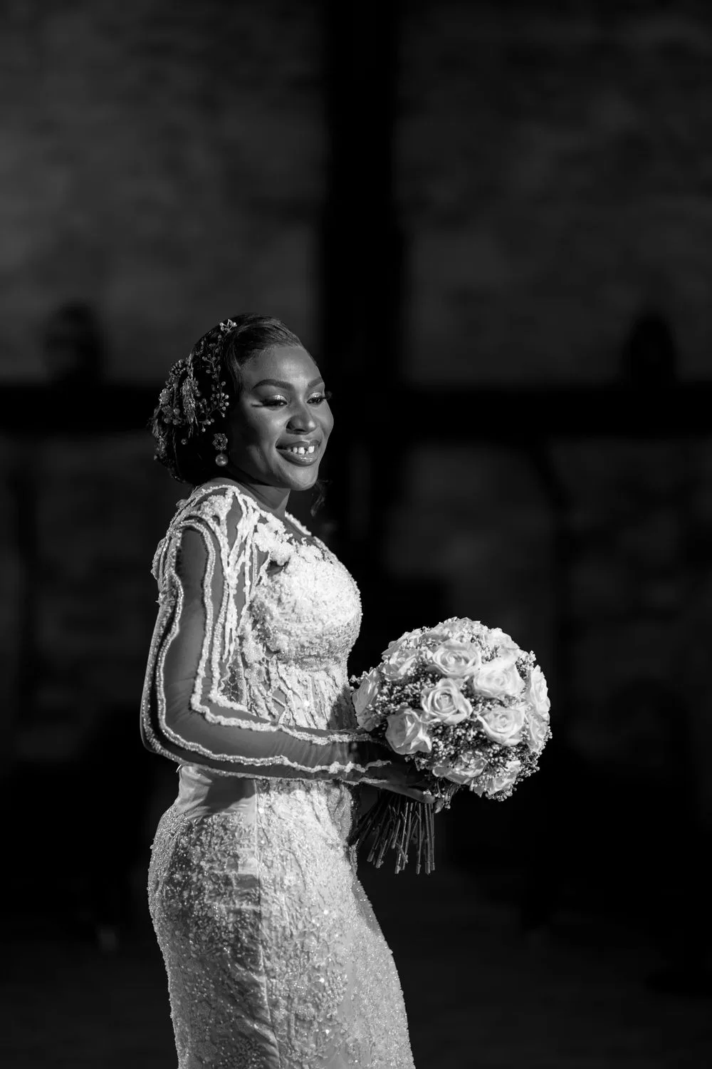A radiant bride in an elegant lace wedding gown holds a large white rose bouquet in this black and white portrait.