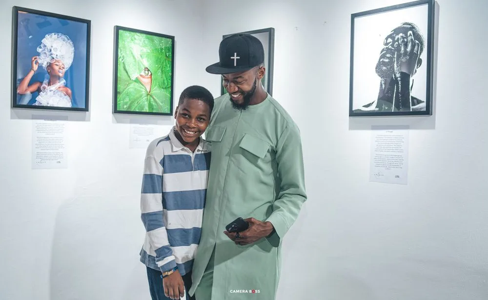 Two people stand together smiling in an art gallery with framed black and white photographs on the white walls.