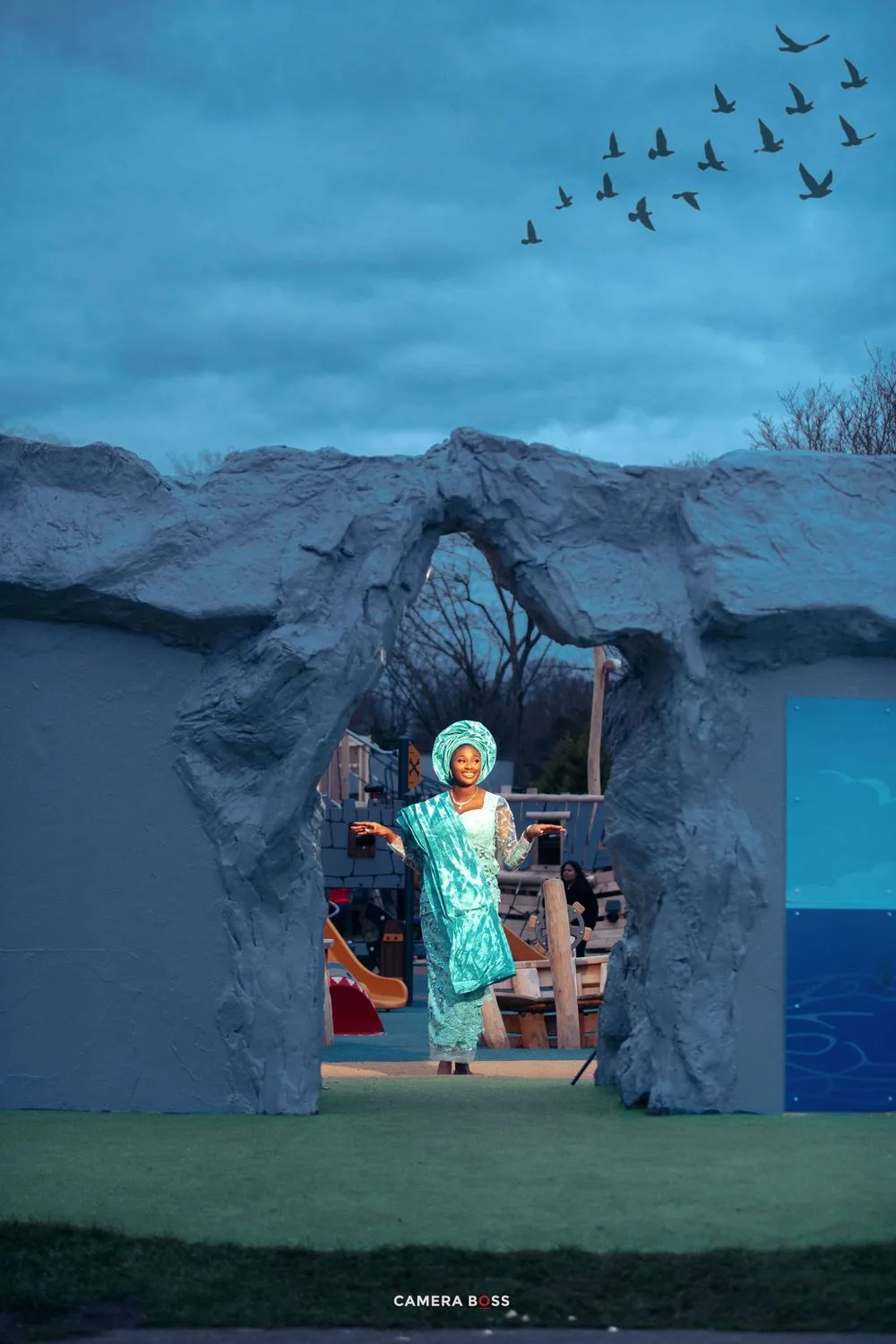 A scenic stage set with a rock archway entrance, mountains in the background, and birds flying in a blue evening sky.