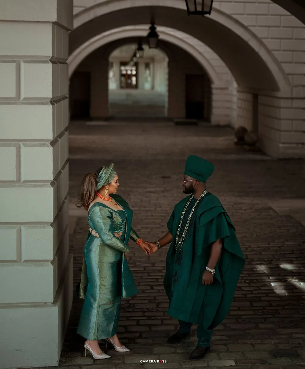 A couple in elegant matching green outfits pose together under stone archways for romantic photos.