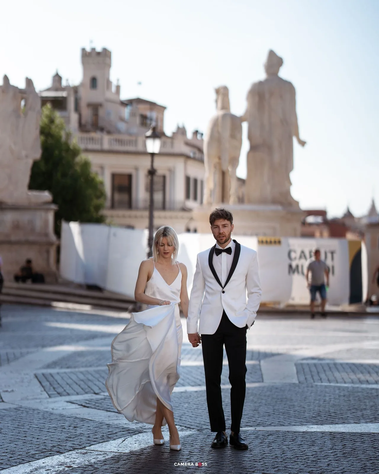 A minimalist artistic photoset of two people in wedding attire posing on cobblestone steps in front of a white building.