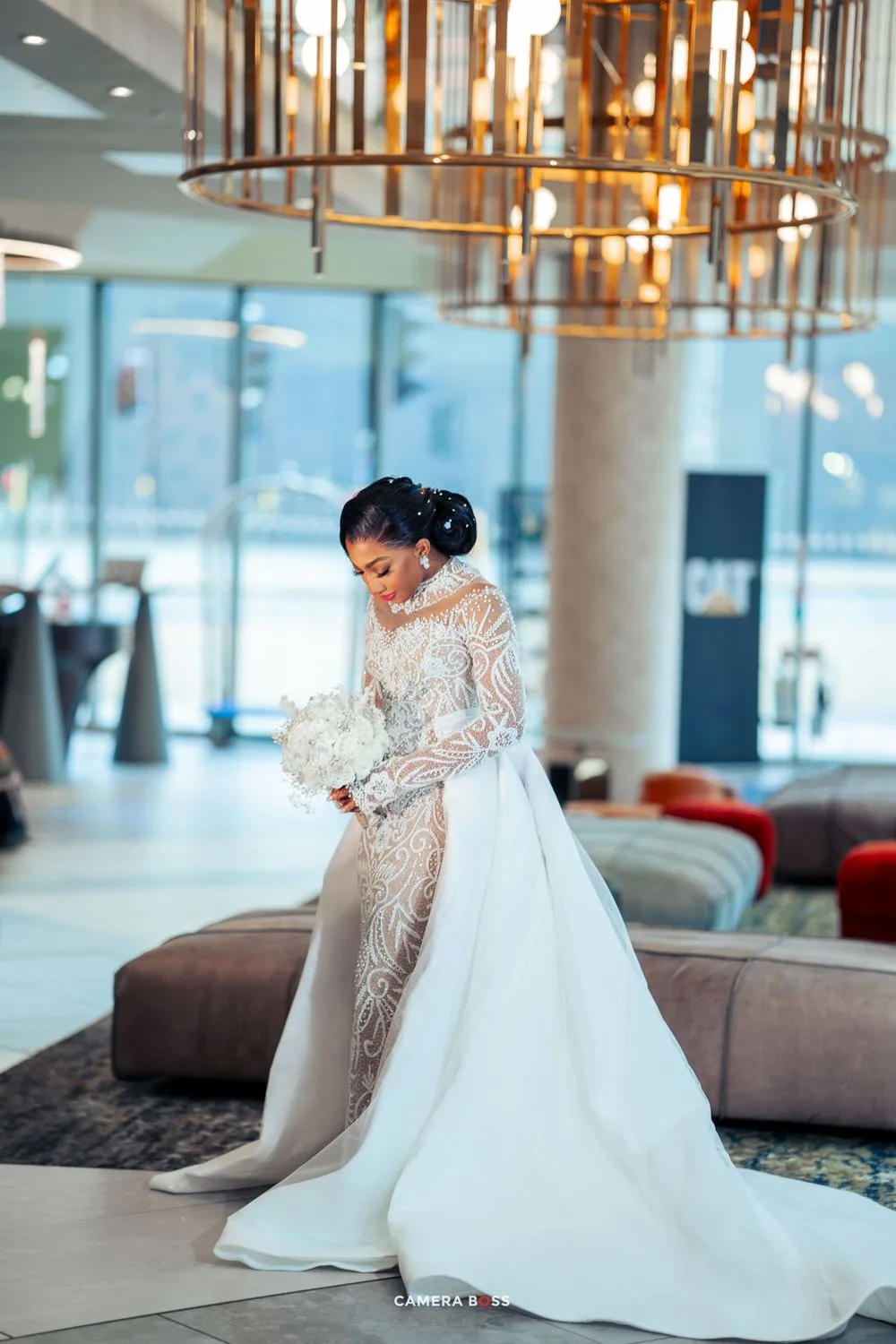Elegant wedding gown with long sleeves, lace bodice and flowing white train in modern hotel lobby with gold lighting.