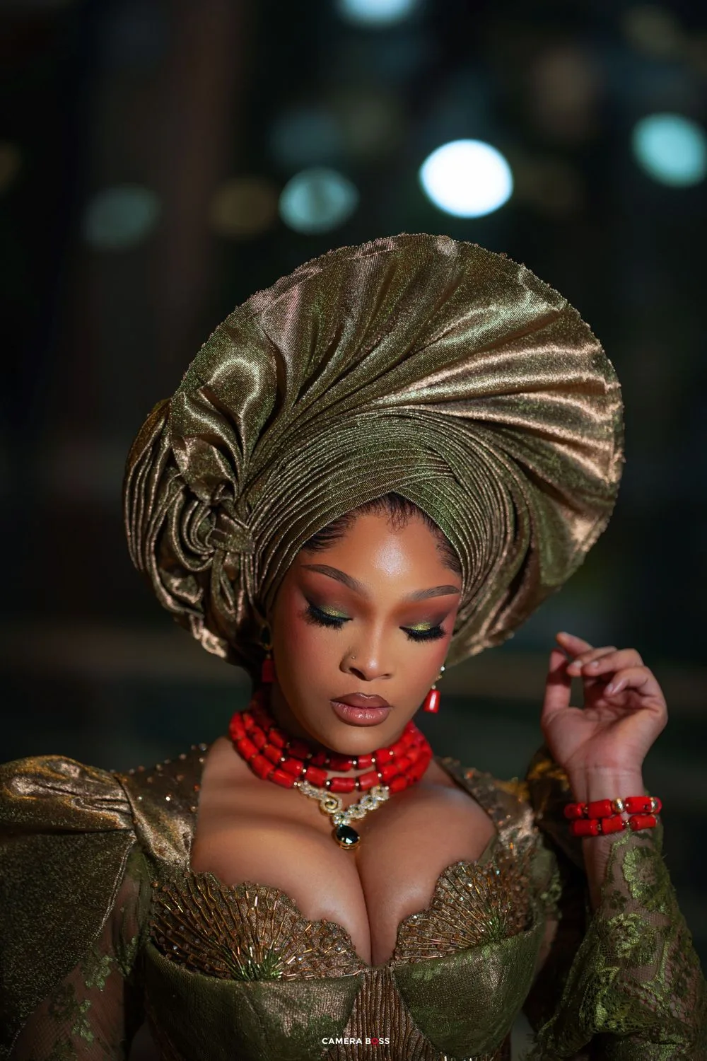 Elegant portrait showing a traditional Nigerian gele headwrap in gold with matching dress and red coral beaded jewelry.