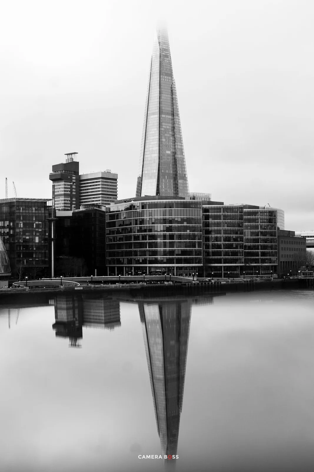 Black and white cityscape of The Shard skyscraper in London reflecting perfectly in the calm Thames River waters below.