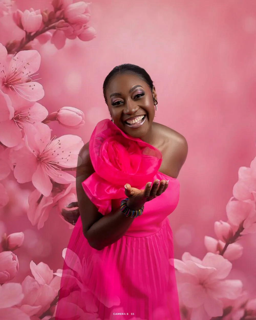 Joyful person wearing bright pink dress against pink floral background with cherry blossoms.