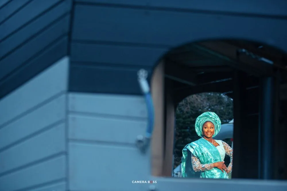 A figure in teal medical scrubs and surgical cap stands in a doorway of a blue building.