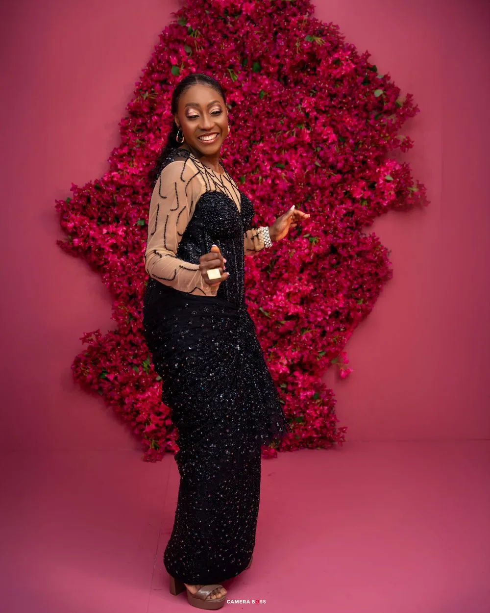 Glamorous photo against vibrant pink floral backdrop featuring sparkly black evening gown paired with tan leather jacket.