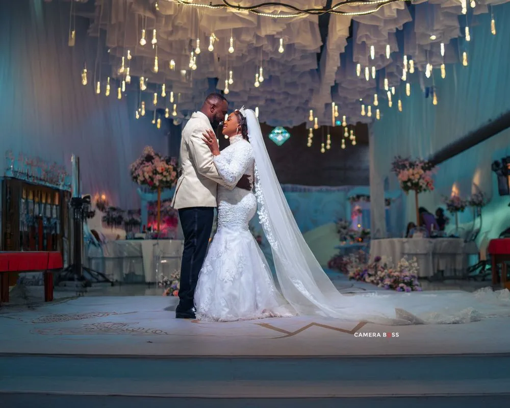 A couple shares a romantic dance moment under suspended hanging lights at an elegant wedding reception.