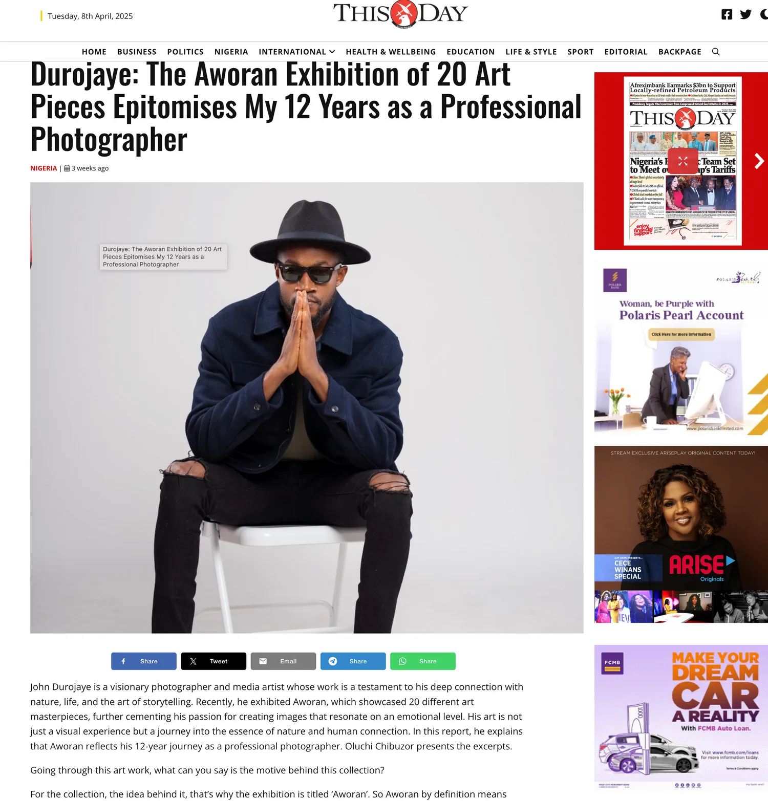 A figure in black attire and fedora hat sits on a white chair against a plain background for a magazine article.