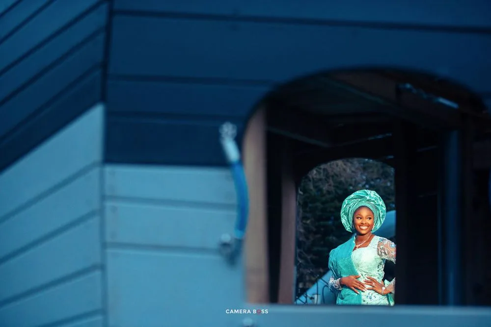 A person wearing a turquoise headscarf stands framed in a doorway of a blue building.