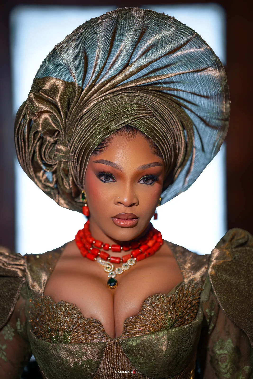 Beautiful African traditional headpiece and formal dress in olive green with red beaded necklace against blurred background.