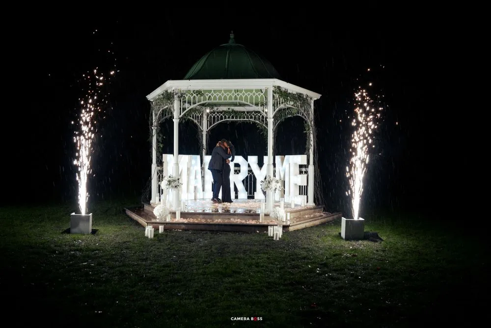 White wooden gazebo decorated with lights and sparkler fountains for a nighttime wedding celebration.