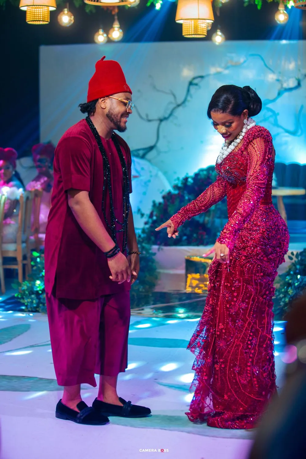 Traditional Nigerian wedding celebration with a joyful dance moment between two people in burgundy and red elegant attire.