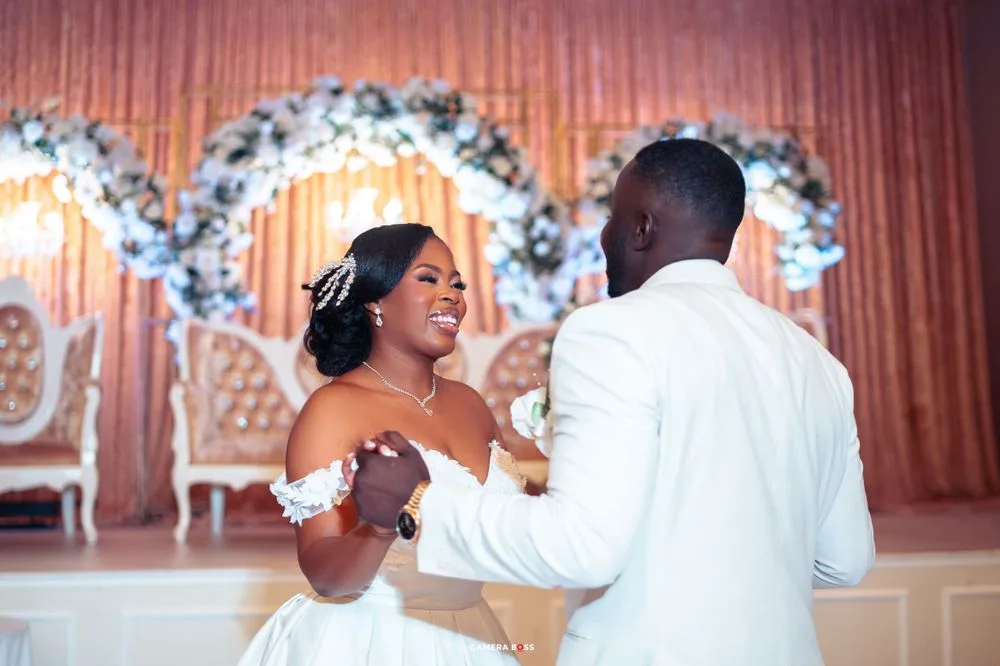 A joyful couple shares their first dance at their wedding reception beneath a floral arch and elegant decor.