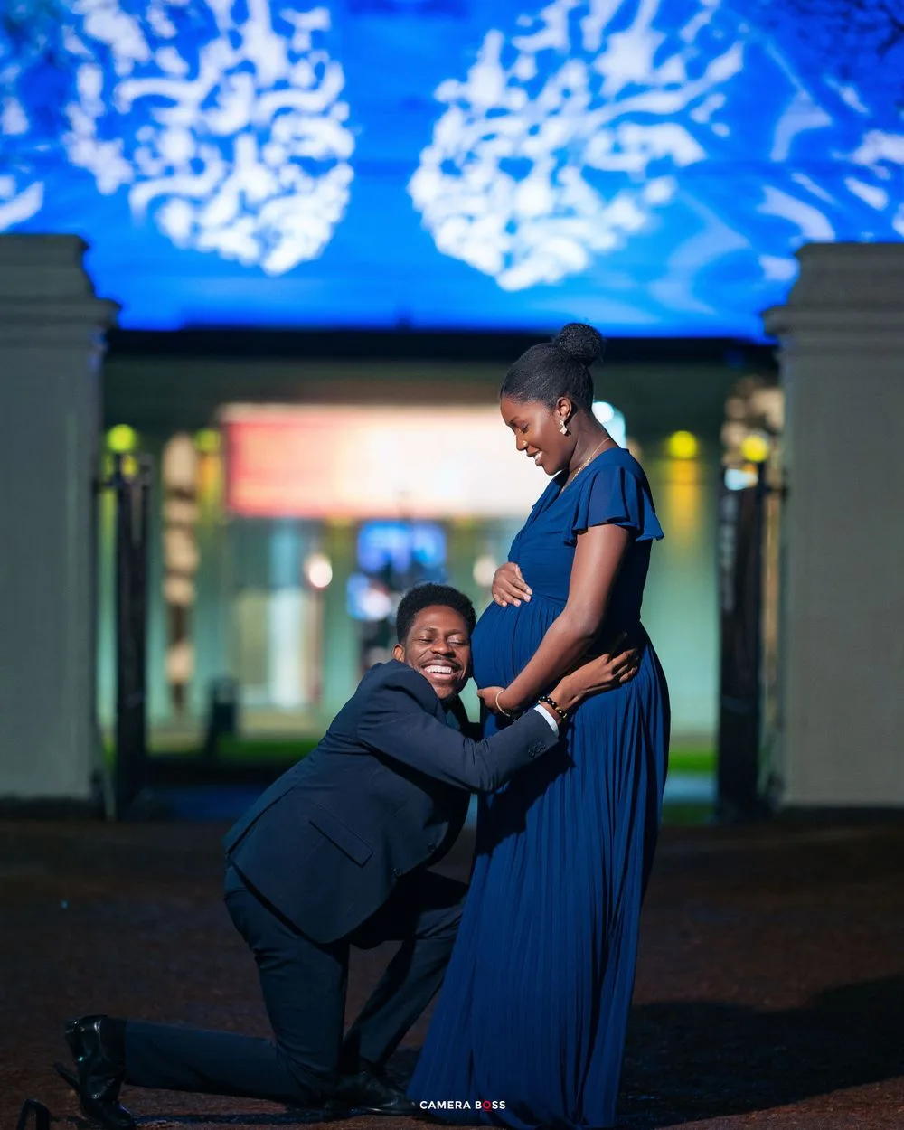 A couple shares an intimate moment at dusk, with dramatic blue lighting and urban architecture in the background.
