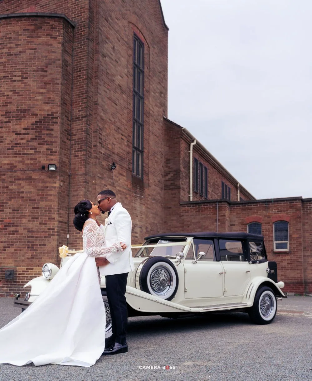 A classic white vintage Rolls Royce parked outside a brick church building on a cloudy day.