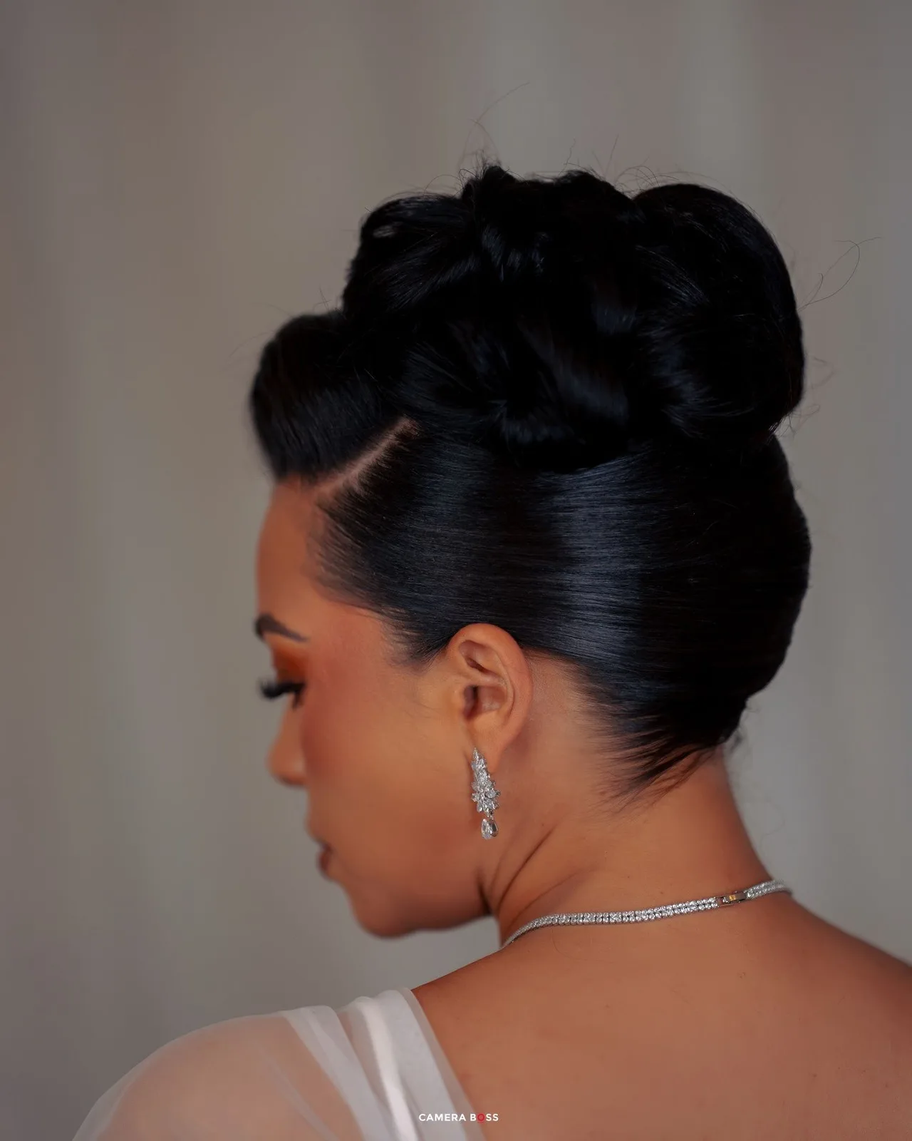 Elegant updo hairstyle shown from side profile view with crystal necklace and earrings for formal occasion.