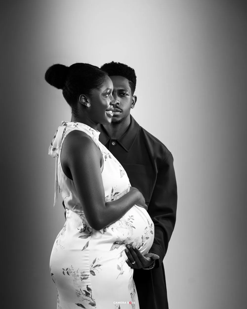 A black and white portrait of a couple in an intimate moment, with a woman in a floral dress and a man in dark clothing.