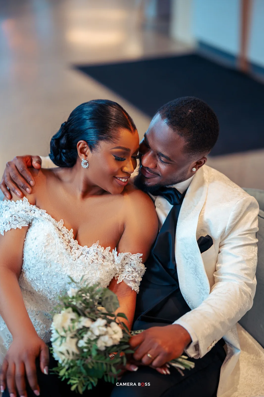 A romantic newlywed couple share an intimate moment together, dressed in a white wedding dress and cream tuxedo jacket.