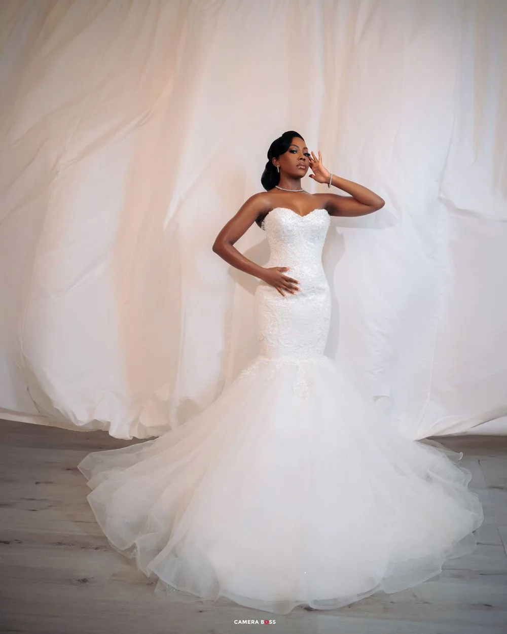 A stunning mermaid-style wedding dress with a sweetheart neckline and flowing tulle train against an ethereal white backdrop.