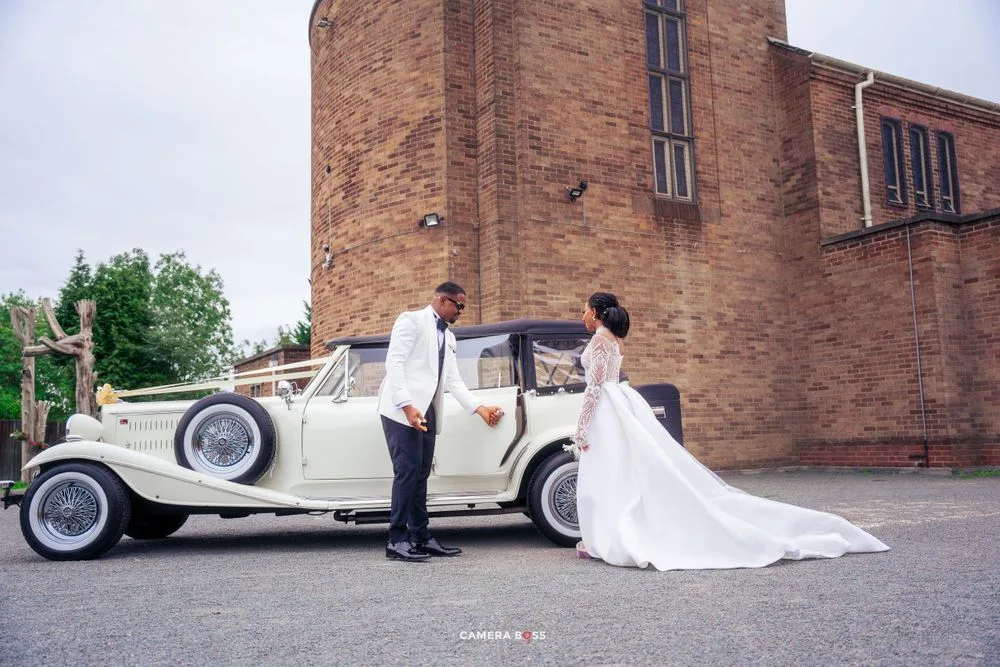 A classic white vintage Rolls Royce parked outside a brick church building during a wedding celebration.