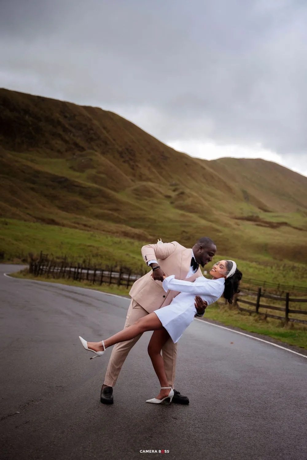 Couple sharing a romantic dip pose on a road with green hills backdrop on their wedding day.