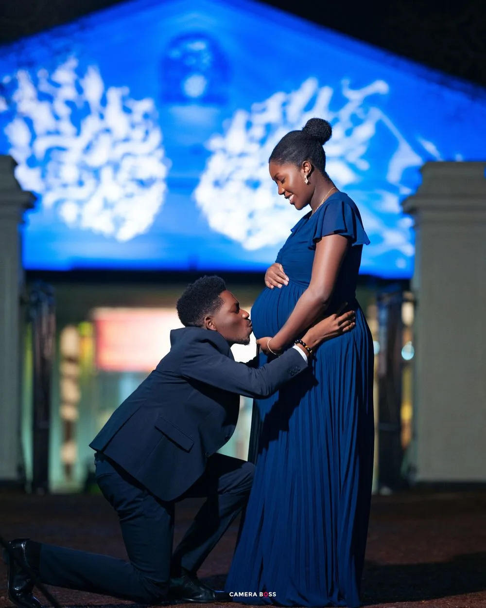 Romantic night scene with couple in evening attire silhouetted against a blue lit architectural backdrop.