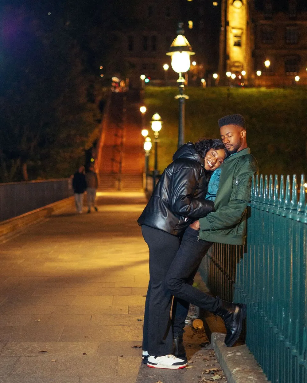 A couple enjoying a romantic nighttime moment together along an illuminated pathway with glowing lampposts.