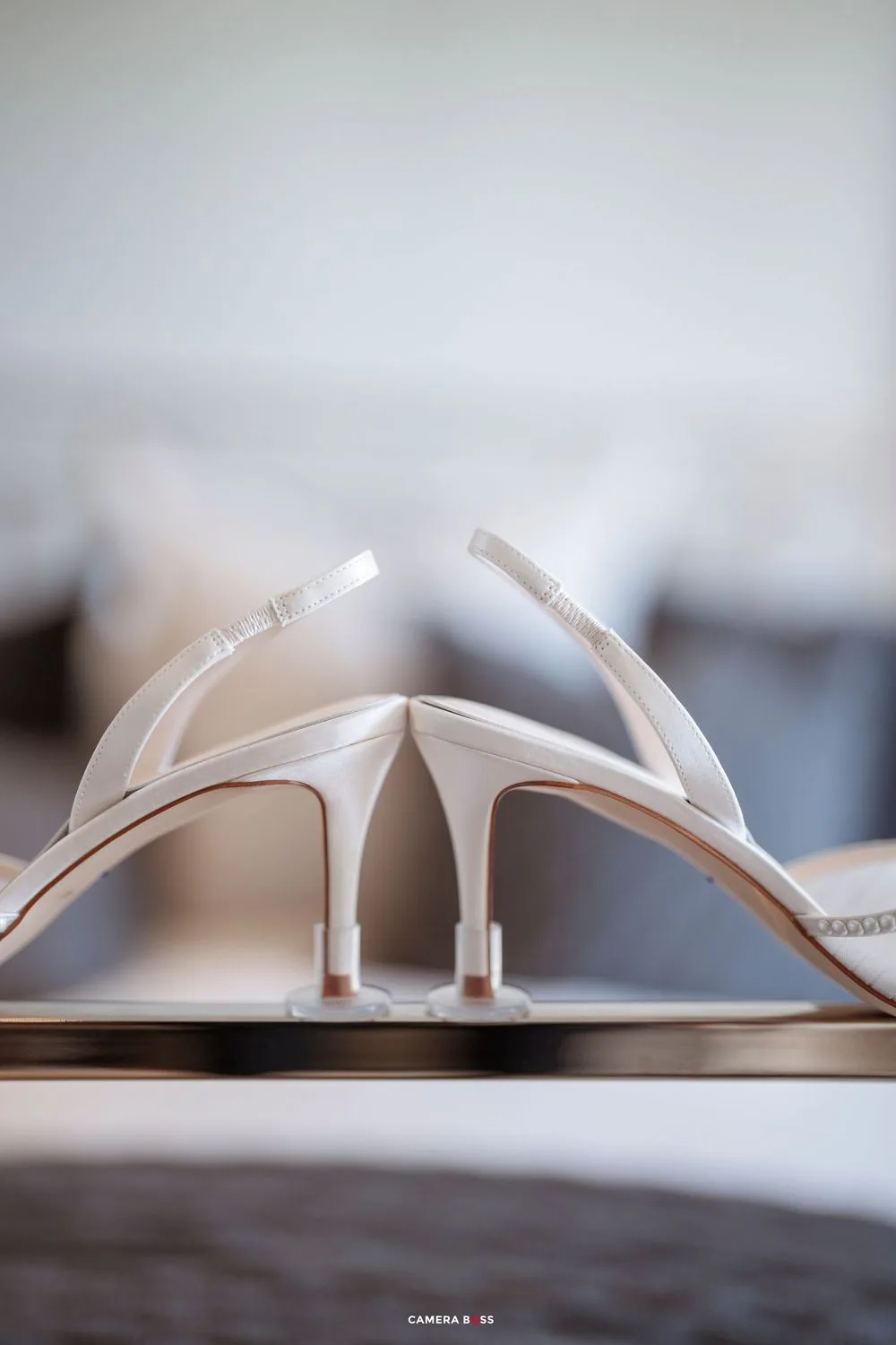 Elegant white bridal stiletto heels with slingback straps displayed on a reflective surface in a softly lit room.