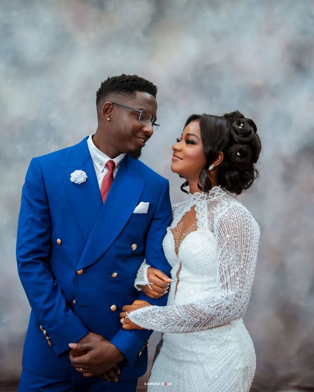 A couple poses for a wedding portrait with the groom in a royal blue suit and the bride in a white lace gown.