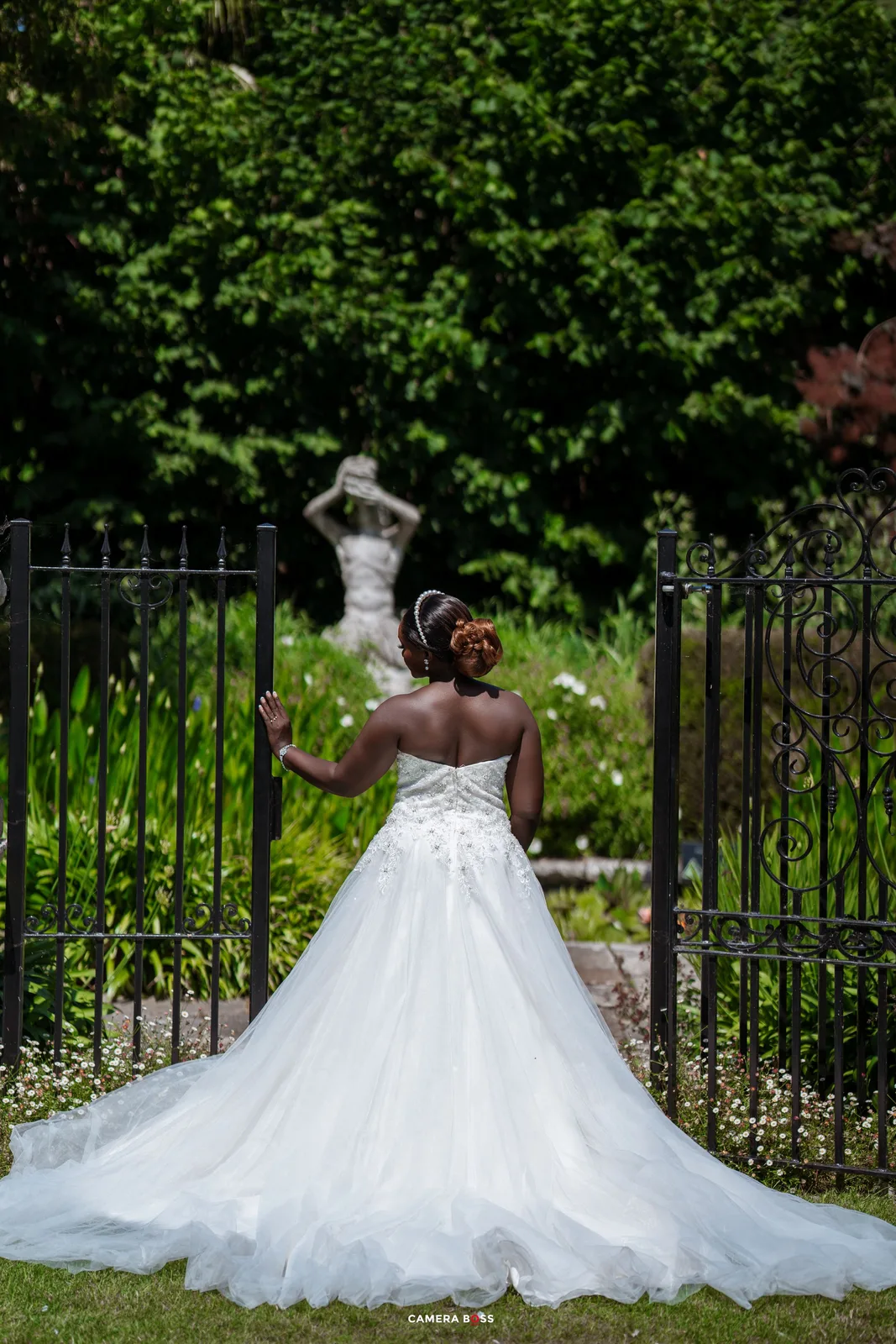 A stunning white wedding dress with full tulle skirt and lace bodice photographed against a garden backdrop with iron gates.