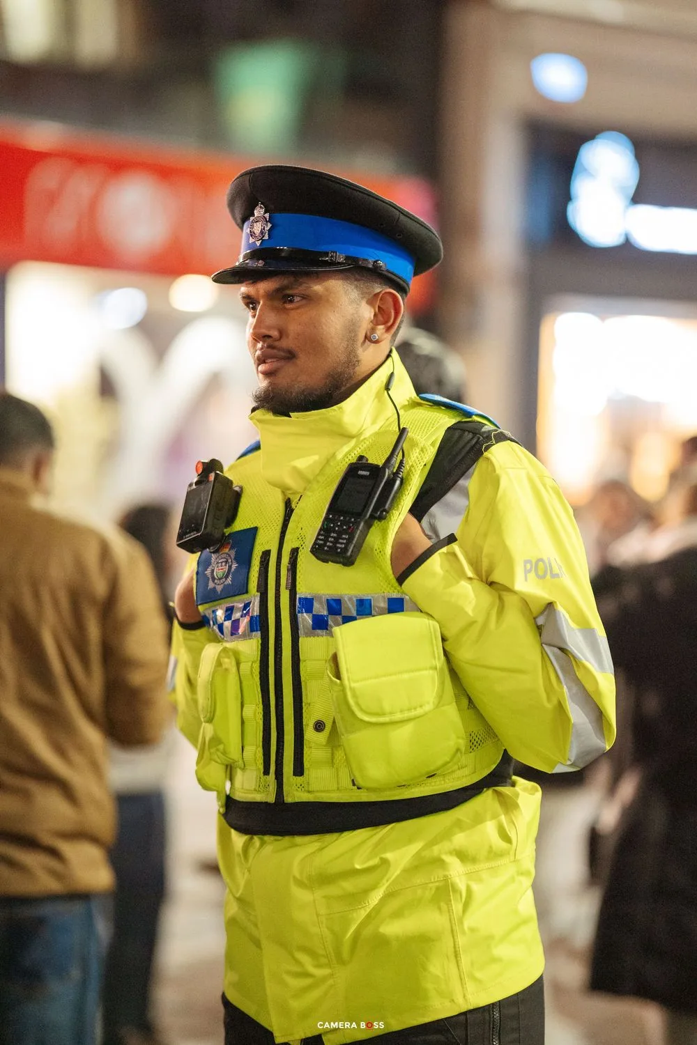 Police officer in high-visibility yellow jacket stands on duty during nighttime patrol.