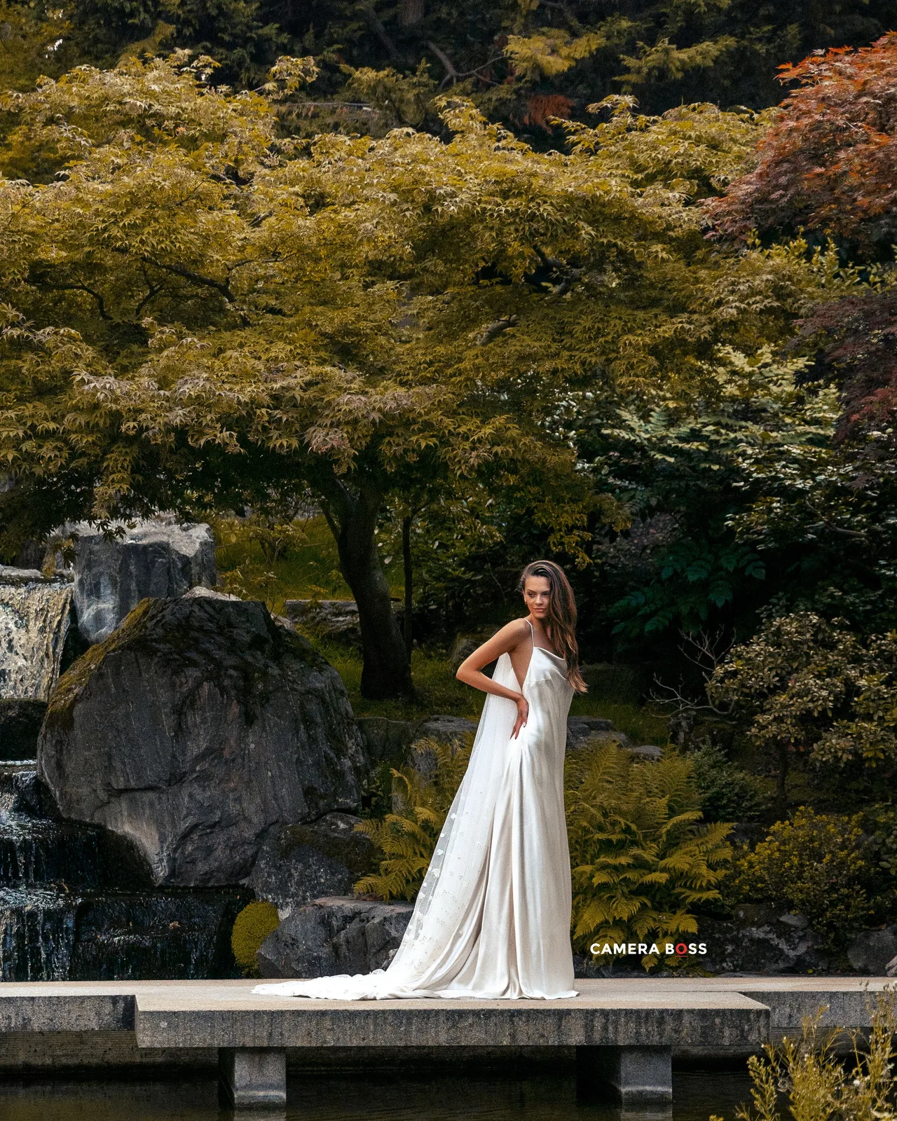 A white wedding dress stands out against lush autumn trees and stone formations in a tranquil Japanese garden setting.