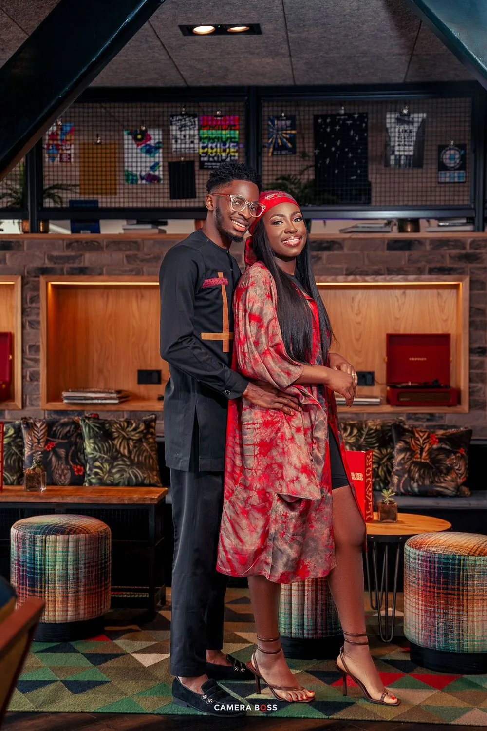A couple in coordinated red and black outfits pose together at a retro-style diner with colorful stools and decorative walls.