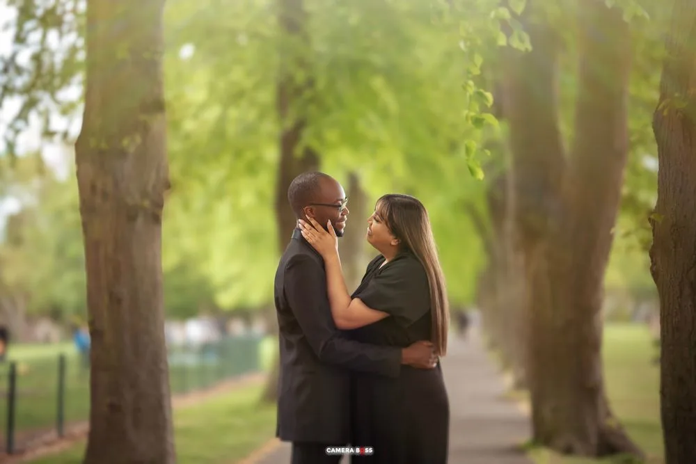 An intimate portrait of a couple embracing on a sunlit garden path surrounded by lush green trees.