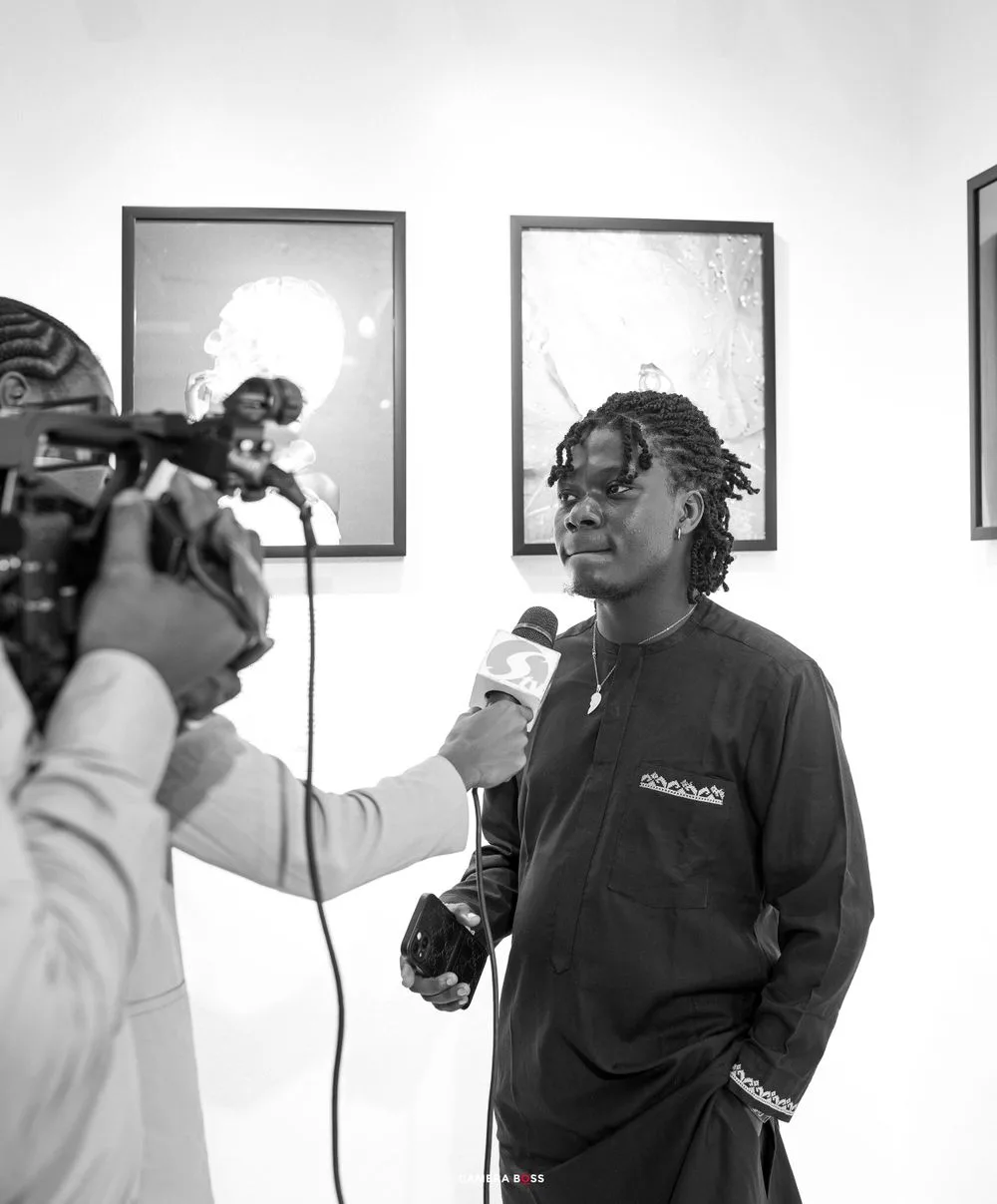 Two people engage in a radio interview or media recording in black and white, with a microphone held between them.
