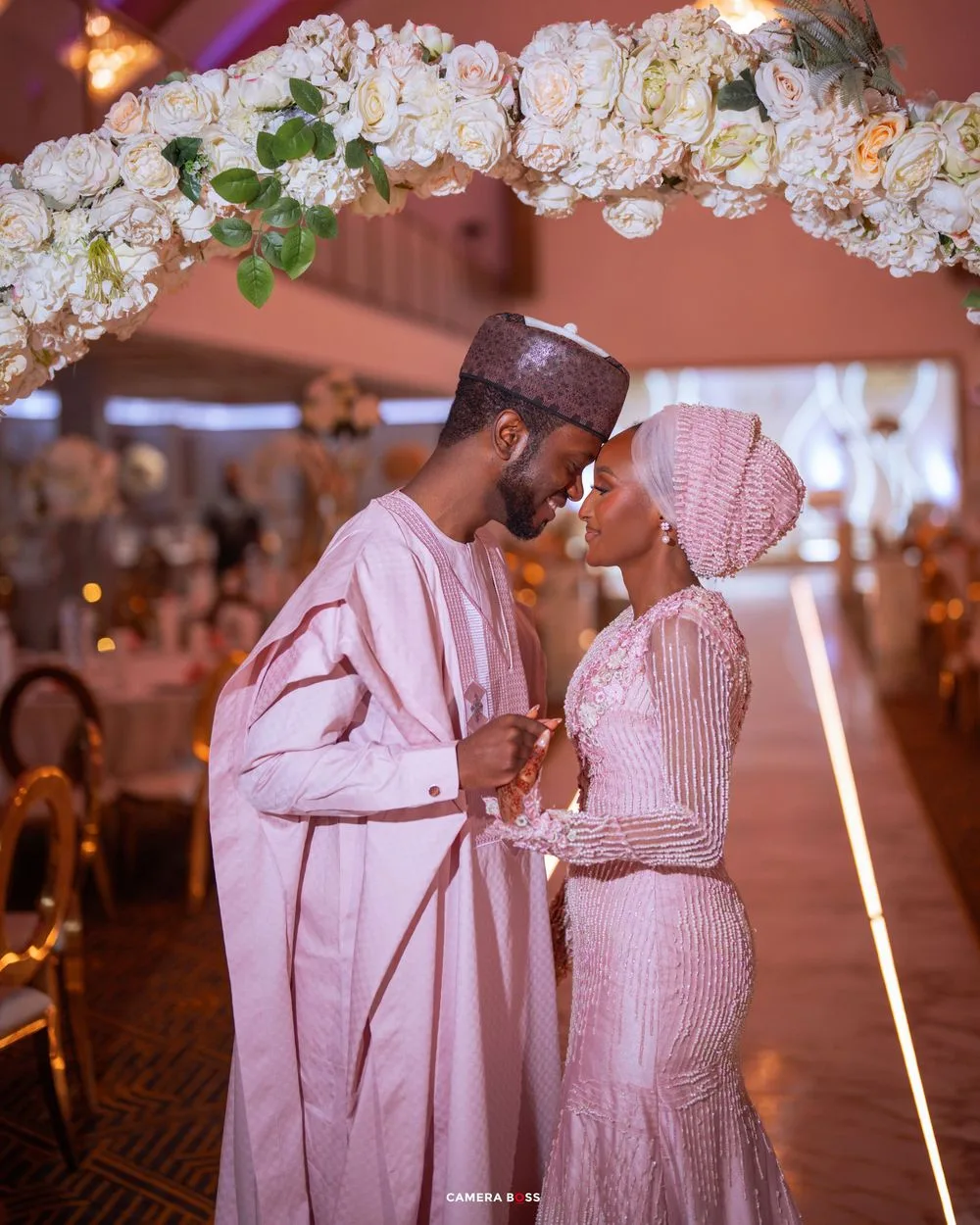A couple shares an intimate moment during a wedding reception with elegant white floral decorations in the background.