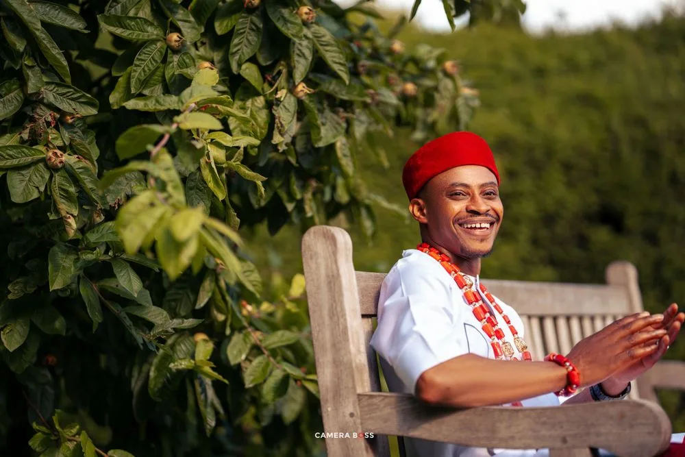 Person wearing red beret and white blouse smiles while sitting on wooden bench in garden setting.
