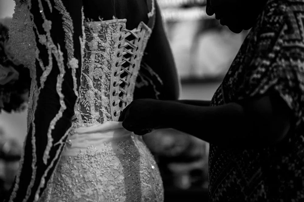 Black and white close-up of a vintage corset with delicate lace details and old-fashioned lacing being tied.