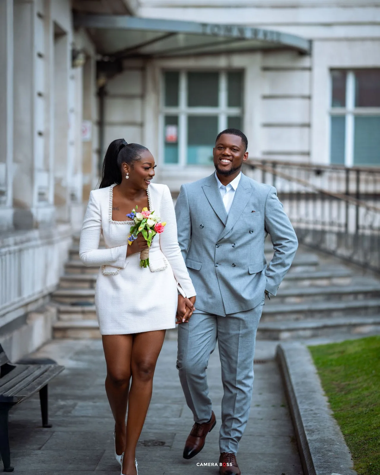 A couple in wedding attire share a joyful moment while walking together on stone steps outside a historic building.