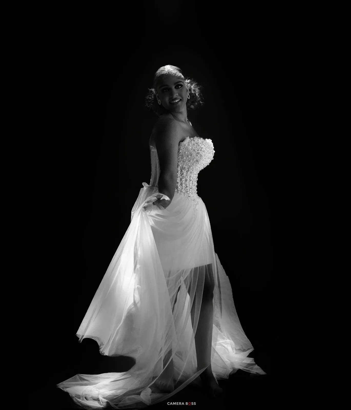 Elegant bride in a white strapless gown poses gracefully in a dramatic black and white studio portrait.