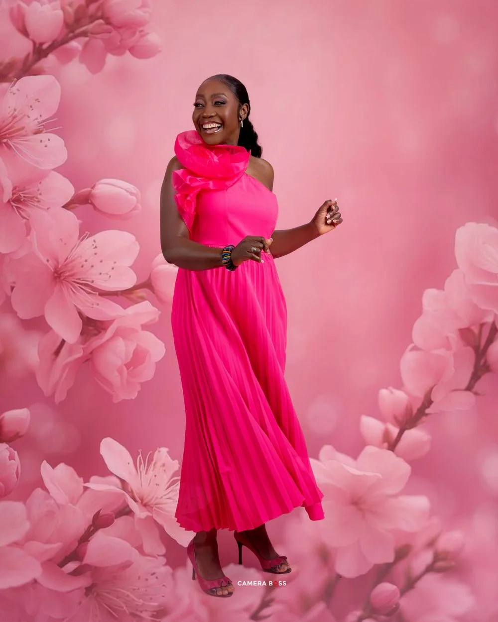 Someone in a vibrant hot pink dress poses against a pink floral backdrop in a studio portrait setting.